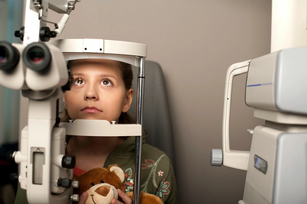 Girl holding a teddy bear while being examined by a slit lamp